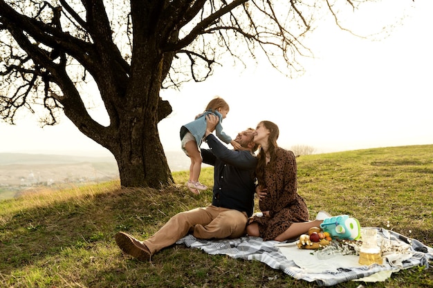 Outdoor recreation of a young married couple with a small child and a pregnant wife the family is sitting on a bedspread and preparing for a picnic in the spring