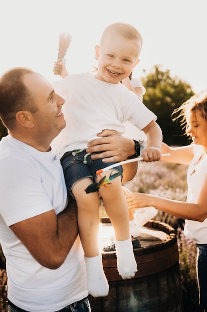 Outdoor shoot of a happy kid in arms of his father against sunset. Happy small son having fun laughing while is holded in hand by his dad.