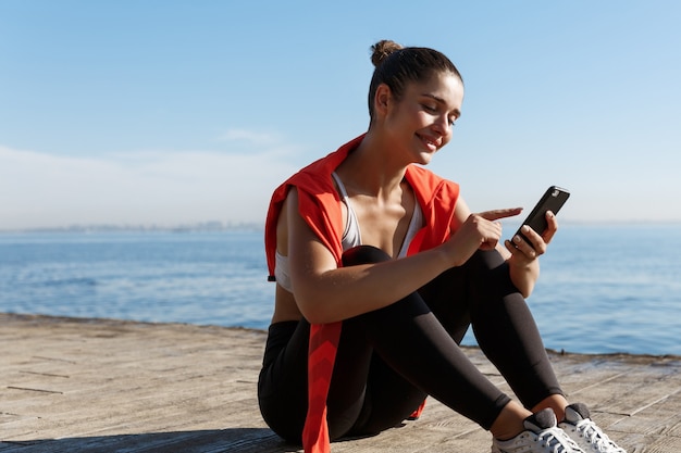 Outdoor shot of attractive sportswoman having a break near sea