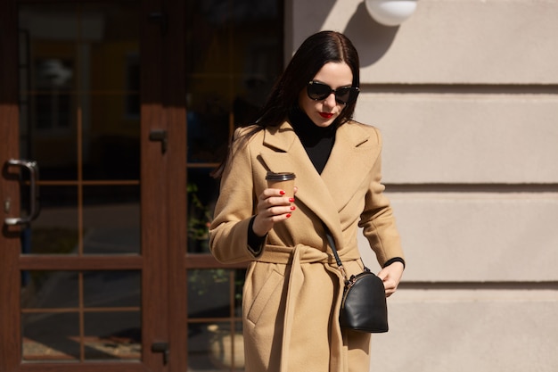 Outdoor shot of beautiful elegant woman wearing beige coat and black sunglasses