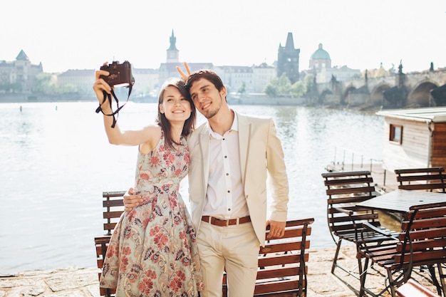 Outdoor shot of happy woman and man embrace each other and pose for making selfie have stroll near wonderful scenery being in good mood enjoys nice weather People and leisure time concept