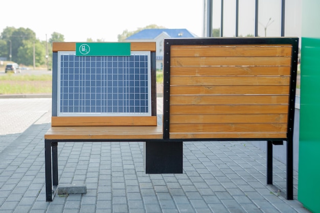 Outdoor shot of wooden bench in park having solar power panel installed USB cabel connected to smartphone