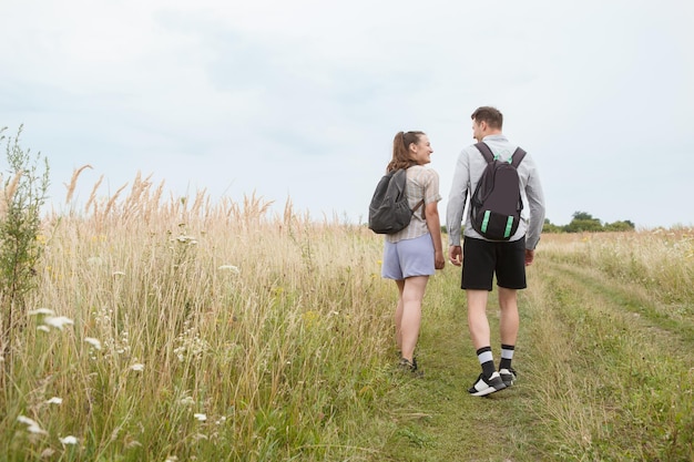 Outdoor shot of young couple in love walking on pathway through grass field Man and woman walking along tall grass field