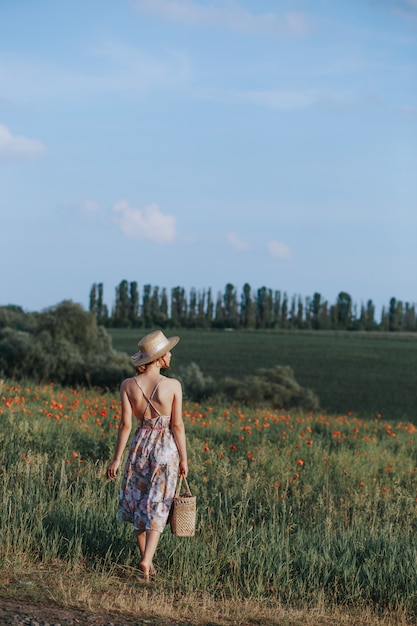 Photo outdoor summer portrait of teen girl with basket strawberries, straw hat. a girl on country road, back view. nature background, rural landscape, green meadow, country style