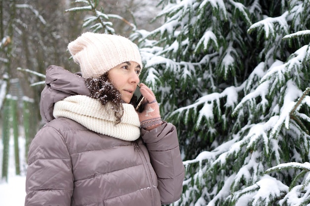 Outdoor winter portrait. Beautiful woman 45 years old talking on a cell phone in a snowy winter park.