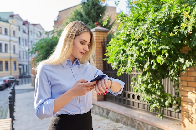 Outdoor young business woman with smartphone looking at wrist watch