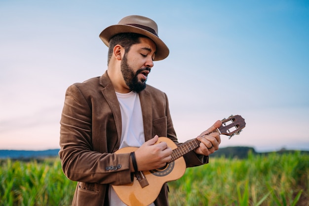 Outdoor of a young Latin American man playing cavaquinho or ukulele. Brazilian musician.