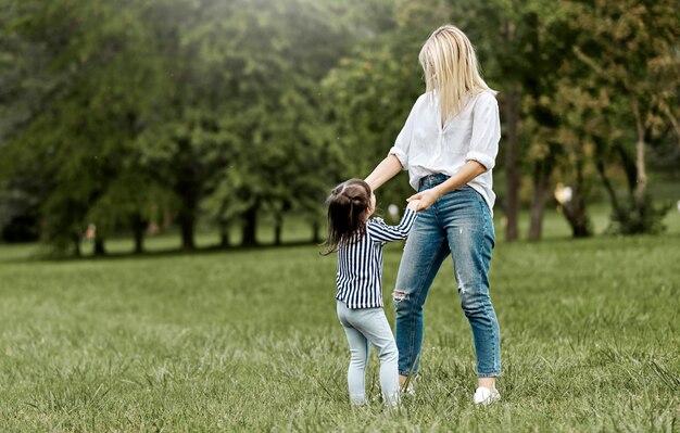 Outdoors image of cute happy little girl playing with her beautiful mother in the park Happy family time together Positive emotion Good relationship between mom and daughter Mothers day concept