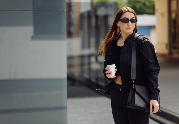 Outdoors lifestyle portrait of stunning brunette girl. Drinking coffee and walking on the city street.