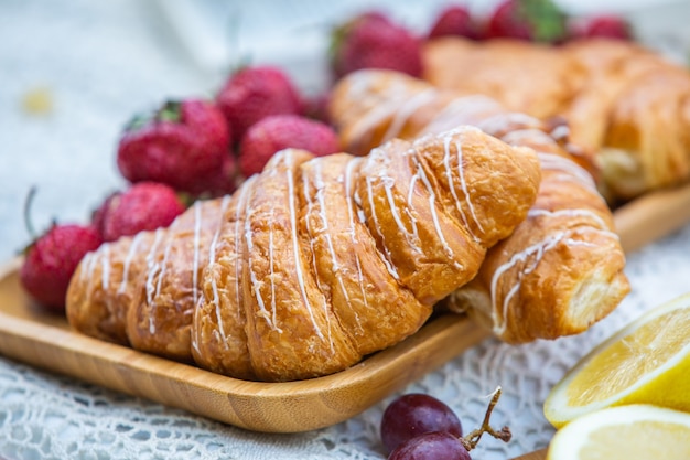 Outdoors picnic in a lush green park with a tasty croissant fruits donuts and wine on grass