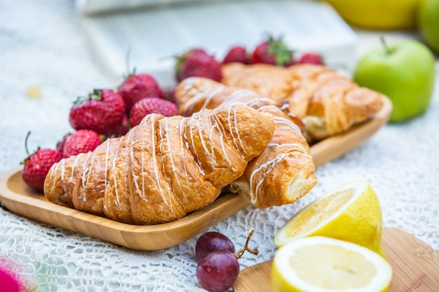 Outdoors picnic in a lush green park with a tasty croissant fruits donuts and wine on grass