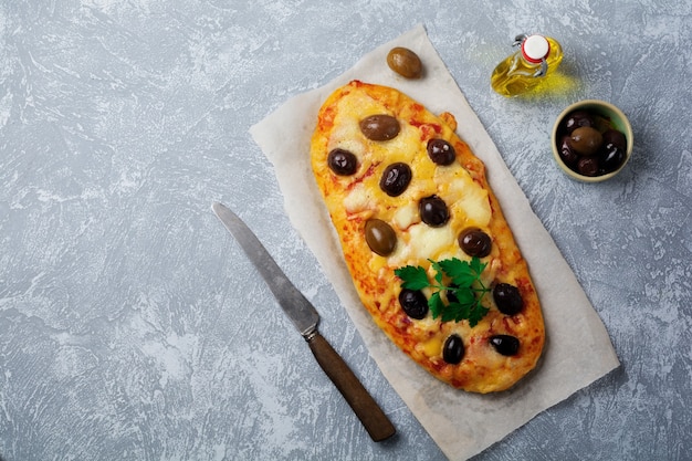 Oval pizza Greek with olives and with tomato on gray concrete.   