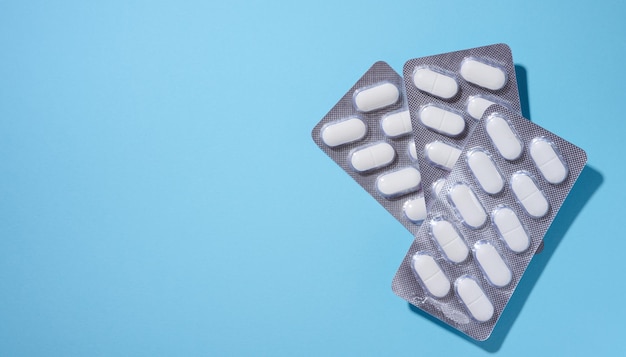 Oval white pills in a gray blister pack on a blue background top view