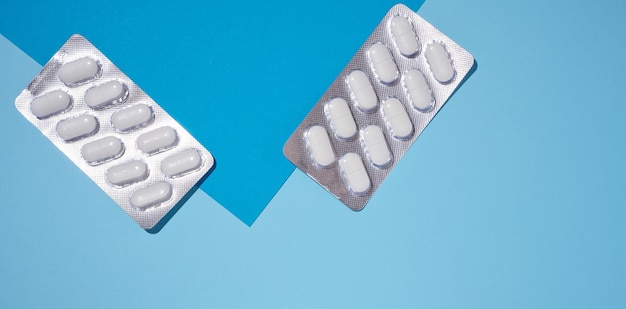 Oval white pills in a gray blister pack on a blue background top view