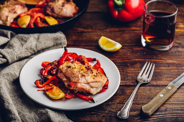 Oven baked chicken thighs with red bell peppers and lemon on white plate