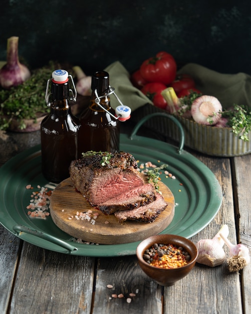 an oven-baked piece of roast beef and two bottles of dark beer on a green country-style iron tray