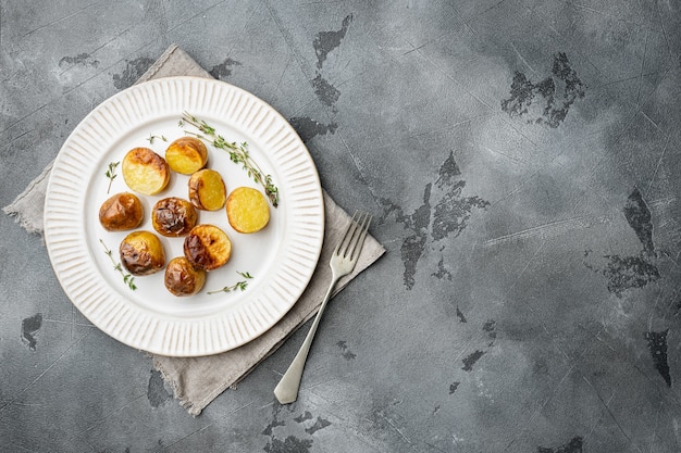 Oven baked potatoes with rosemary set, on plate, on gray stone table background, top view flat lay, with copy space for text