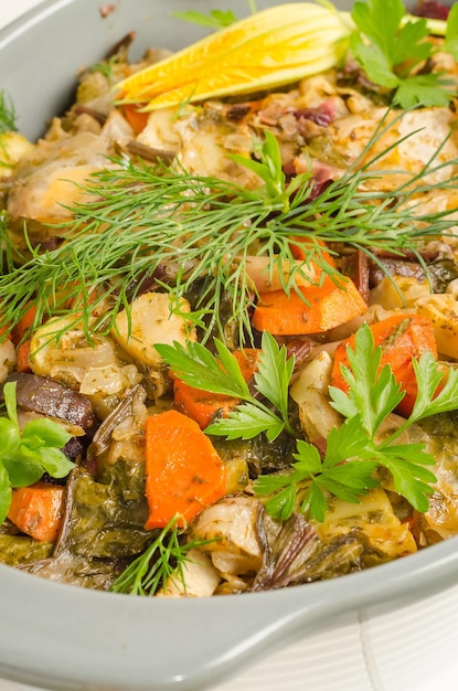 Oven baked vegetables with herbs in a baking dish on a white wooden background