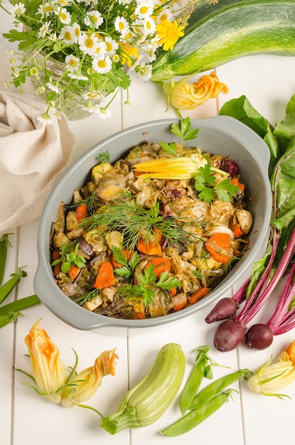 Oven baked vegetables with herbs in a baking dish on a white wooden background