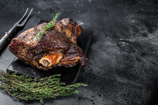 Oven Roasted lamb mutton whole leg with thyme. Black background. Top view. Copy space.