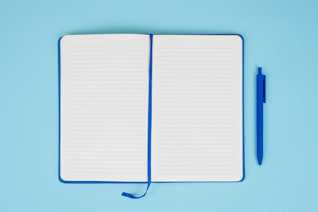 Above overhead close up view photo image of notepad with empty pages and pen isolated over pastel color blue background