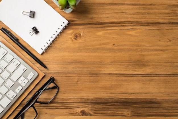 Overhead above flat lay view photo of computer keyboard flowerpot clear spiral notebook eyeglasses isolated light brown backdrop with place for text