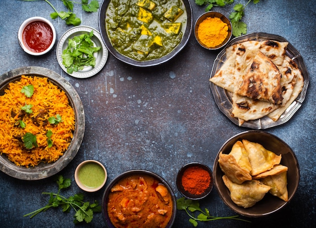 Overhead of Indian traditional dishes and appetizers: chicken curry, pilaf, naan bread, samosas, paneer, chutney on rustic background. Table with choice of food of Indian cuisine, space for text