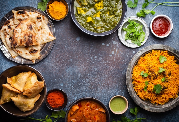 Overhead of Indian traditional dishes and appetizers: chicken curry, pilaf, naan bread, samosas, paneer, chutney on rustic background. Table with choice of food of Indian cuisine, space for text