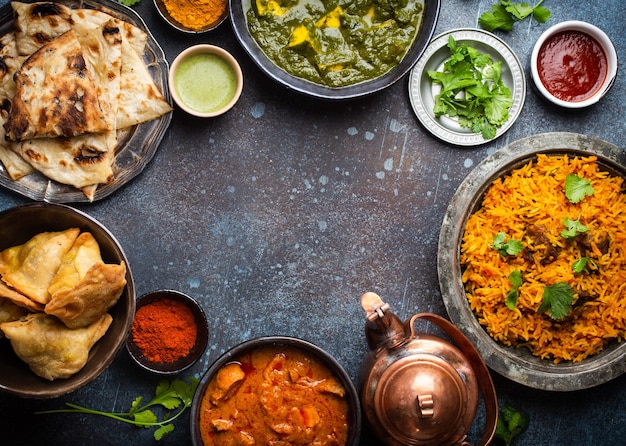 Overhead of Indian traditional dishes and appetizers: chicken curry, pilaf, naan bread, samosas, paneer, chutney on rustic background. Table with choice of food of Indian cuisine, space for text