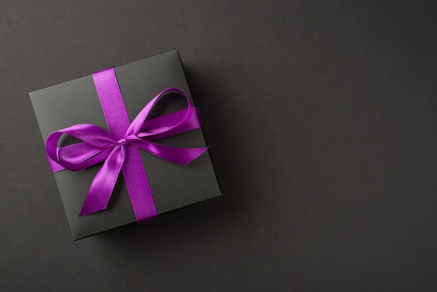 Overhead photo of black giftbox with violet ribbon wrapped as bow isolated on the black background