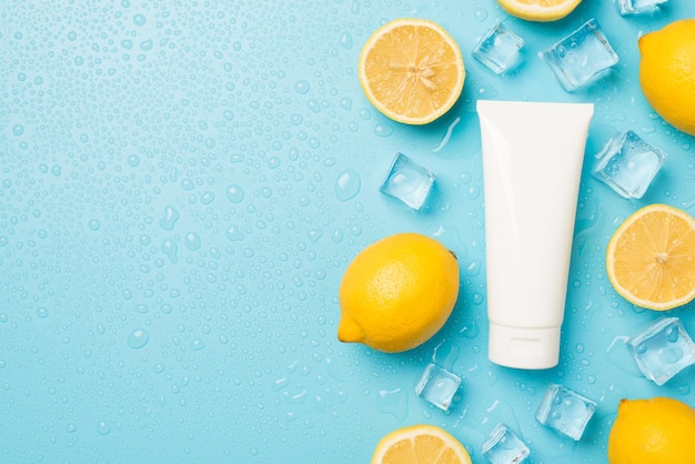 Overhead photo of lemons cubes of ice drops and white tube of cream isolated on the blue background with empty space