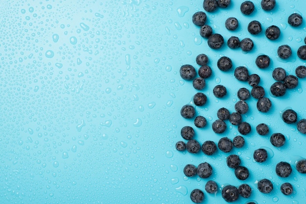 Overhead photo of pile of blueberries and drops of water isolated on the blue background with empty space