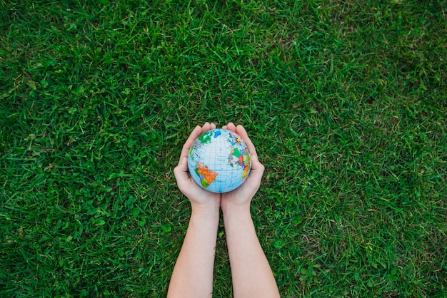 An overhead's view of hands holding globe over green grass