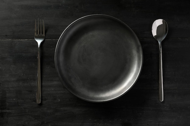 Overhead shot Modern black dining table setting with empty black plate fork and spoon flat lay