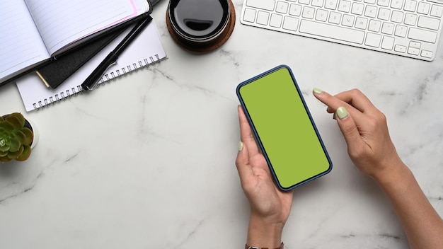 Overhead shot  of woman holding smart phone with green screen on marble background