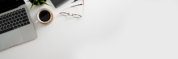 Overhead shot of workspace with laptop, glasses, coffee cup and copy space on white wooden desk