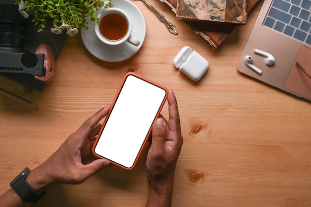 Overhead sot of man holding mock up mobile phone with blank screen on wooden table.