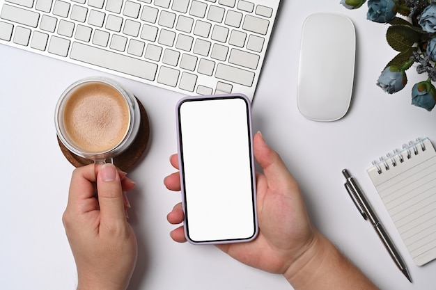 Overhead view businessman holding coffee cup and using mobile phone at white office desk.