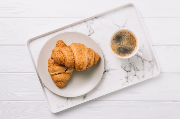 Overhead view of coffee cup and plate of croissant bread in tray