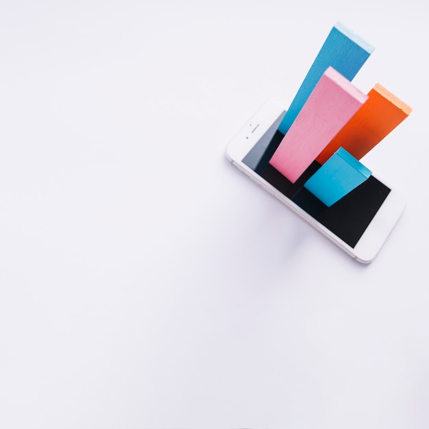 Overhead view of colorful bars popping out from smartphone screen on white backdrop