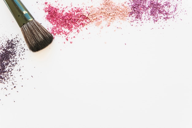 An overhead view of colorful cosmetic face powder and make-up brush on white backdrop