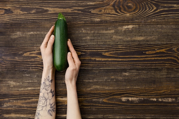 Overhead view of fresh green zucchini in hands over wooden background