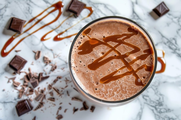 Overhead view of a frothy chocolate milkshake artistically topped with caramel drizzle on a marble background with chocolate pieces