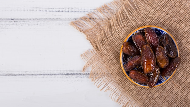 An overhead view of juicy ripe dates bowl on sack cloth over the white desk