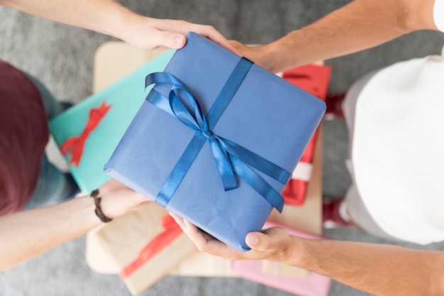 Overhead view of male friend's holding blue wrapped gift box with tied ribbon