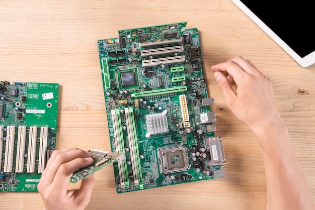 Photo overhead view of male it technician repairing circuit board on wooden table