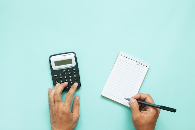 Overhead view of man hands using calculator and paper note on blue colour background with copy space