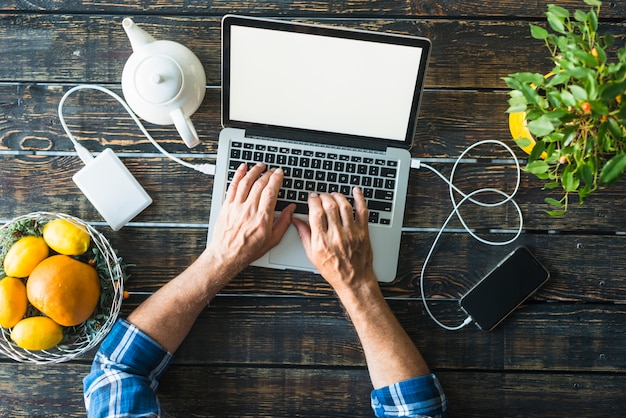 Overhead view of man's hand typing on laptop charged with power bank