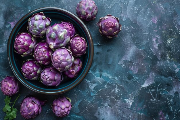 An overhead view of raw purple artichokes in a dark ceramic bowl placed on a textured surface