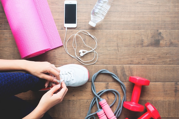 Overhead view of sport woman tying shoe with mobile phone and sport equipments